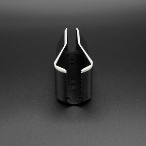 May include: A black and white plastic cup holder. The cup holder has a cylindrical base with a white rim and a white interior. The holder is designed to hold a cup or bottle. The background is a solid black.