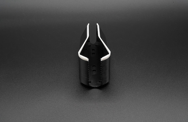 May include: A black and white plastic cup holder. The cup holder has a cylindrical base with a white rim and a white interior. The holder is designed to hold a cup or bottle. The background is a solid black.
