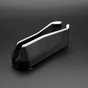 May include: A black and white plastic object with a curved design. The object has a rectangular body with a white trim along the top edges. The item is set against a dark background.