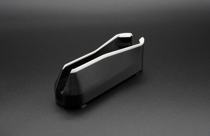 May include: A black and white plastic object with a curved design. The object has a rectangular body with a white trim along the top edges. The item is set against a dark background.