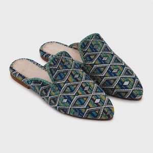 Puede incluir: Un par de zapatillas sin talón con un estampado geométrico en tonos azules, verdes, amarillos y blancos. Las zapatillas tienen un interior beige y una suela marrón. El diseño presenta un patrón de diamantes repetido.