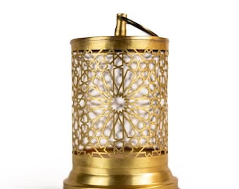 May include: A gold-colored metal lantern with a cylindrical shape and intricate geometric cutouts. The lantern has a base, a top, and a handle. The cutouts create a star-like pattern. The lantern is likely used for decorative purposes.