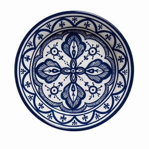 May include: A round, white ceramic plate with a blue floral design. The plate features a central motif of stylized leaves and a border of repeating floral patterns. The rim is a solid blue, and the plate is suitable for serving food.