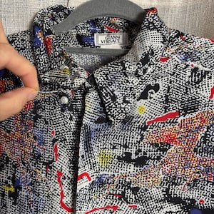 May include: A button-down shirt with a black and white abstract pattern, accented with red, blue, and yellow splashes. The shirt features the "GIANNI VERSACE" label on the collar.