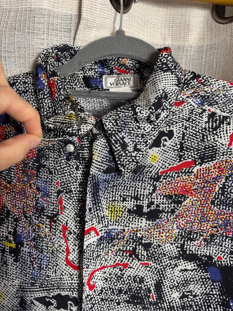 May include: A button-down shirt with a black and white abstract pattern, accented with red, blue, and yellow splashes. The shirt features the "GIANNI VERSACE" label on the collar.
