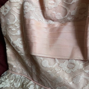 May include: A pink and white lace dress with a satin bodice. The dress has a ruffled hem and a delicate floral pattern.