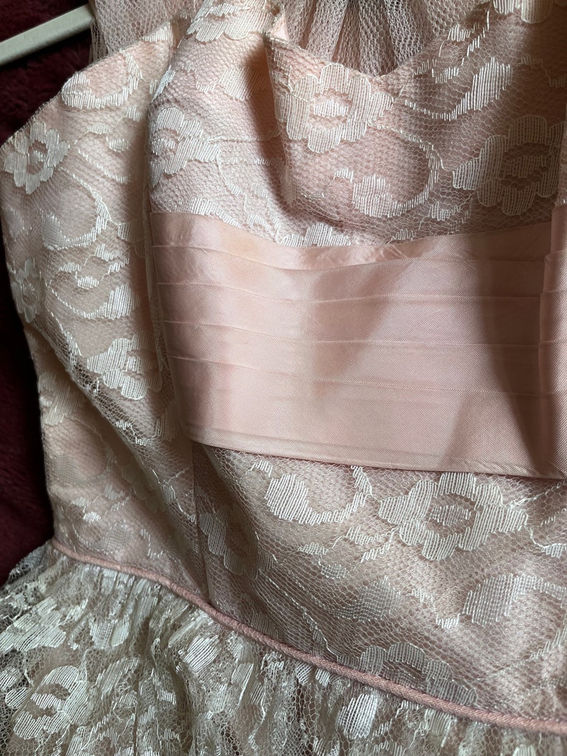 May include: A pink and white lace dress with a satin bodice. The dress has a ruffled hem and a delicate floral pattern.