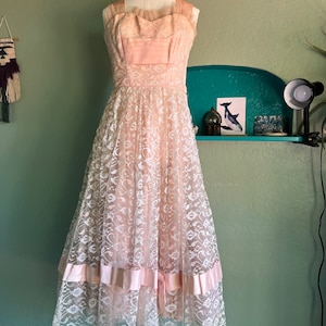 May include: A vintage pink and white lace dress with a sweetheart neckline and a full skirt. The dress has a satin ribbon at the waist and a layered skirt.