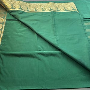 May include: A solid green fabric textile featuring a wide border with a repeating gold paisley pattern. The fabric includes a section with horizontal gold stripes, showcasing a smooth texture and a vibrant emerald green color throughout the piece.