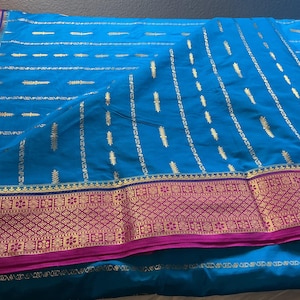 May include: A bright blue fabric featuring a wide magenta border with intricate gold metallic patterns. The main body of the textile is decorated with vertical rows of small, repeating gold leaf-shaped motifs and thin gold metallic stripes.