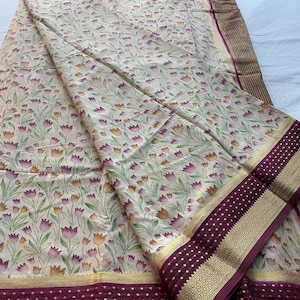 May include: A cream-colored fabric featuring a repeating pattern of small orange and purple tulips with green stems. The textile is bordered by a wide, deep maroon band decorated with gold-colored geometric patterns and small dots.