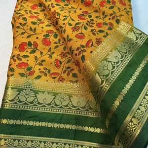 May include: A yellow fabric featuring a repeating pattern of small red flowers and green leaves. The fabric includes a wide, dark green border decorated with intricate gold metallic floral and geometric designs along the edges and center.
