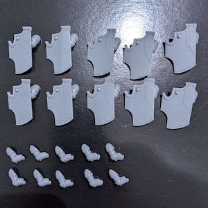 May include: A set of 12 grey plastic miniature parts for a model kit. The parts include 10 shields and 2 arms.