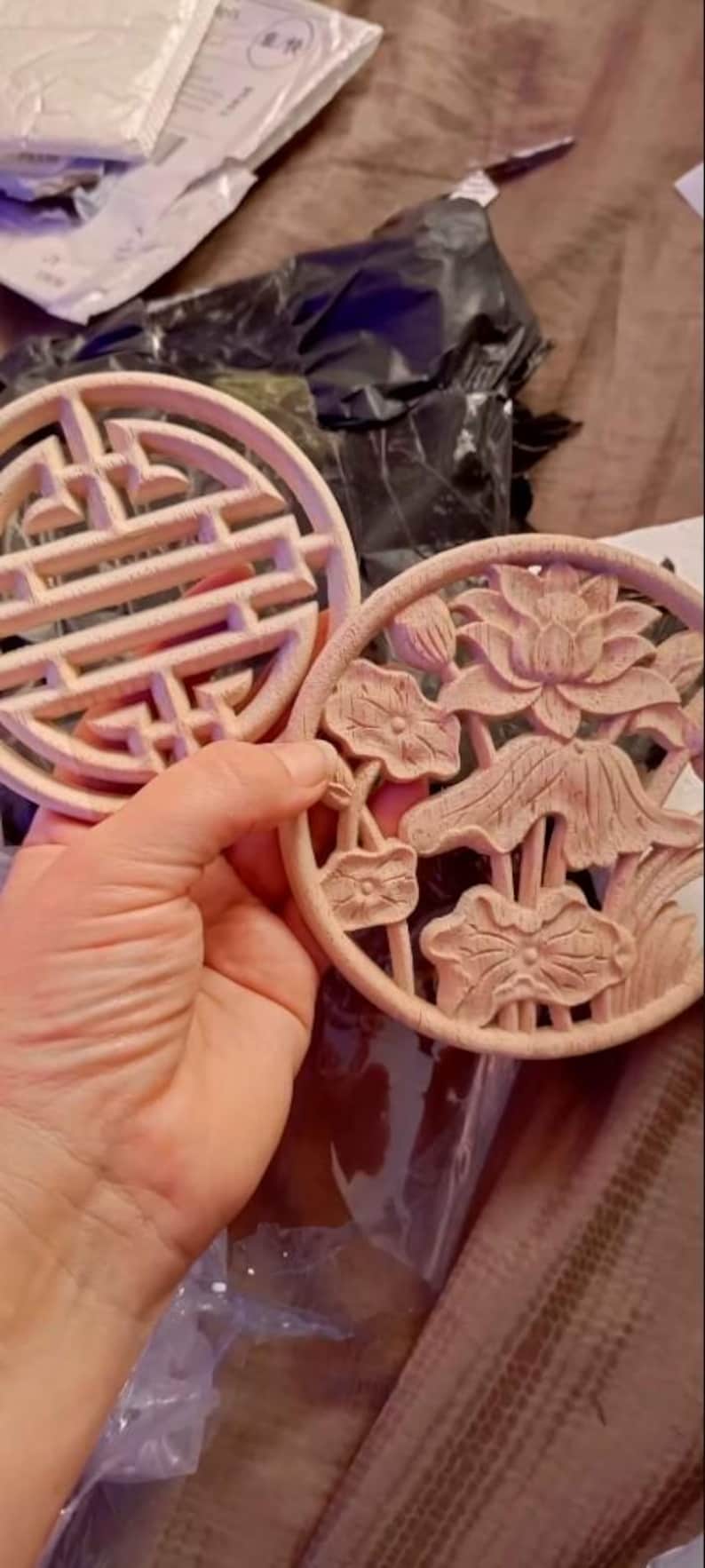 May include: Two round, wooden coasters with intricate designs. One coaster features a geometric pattern, while the other has a floral design with carved lotus flowers.