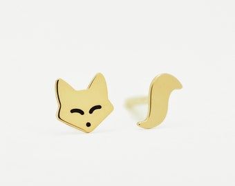 May include: A pair of gold fox earrings. One earring features a fox head with closed eyes and a small mouth. The other earring features a fox tail.