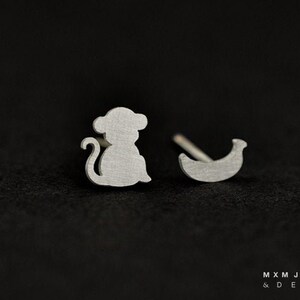 May include: A pair of silver earrings, one shaped like a monkey and the other shaped like a banana.