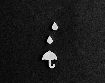 May include: White paper cutouts of raindrops and an umbrella on a black background. The text "MXM JEWELRY & DESIGN" is at the bottom of the image.