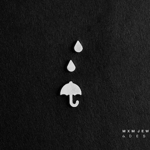 May include: White paper cutouts of raindrops and an umbrella on a black background. The text "MXM JEWELRY & DESIGN" is at the bottom of the image.