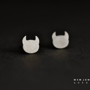 May include: A pair of silver earrings with a small, minimalist devil head design.