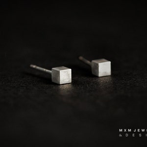 Könnte beinhalten: Ein Paar silberne Würfel-Ohrstecker. Die Ohrringe sind klein und minimalistisch und perfekt für den Alltag.