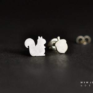 Peut inclure: Une paire de boucles d'oreilles en argent avec un motif d'écureuil et de gland. Les boucles d'oreilles sont petites et délicates, parfaites pour un usage quotidien.