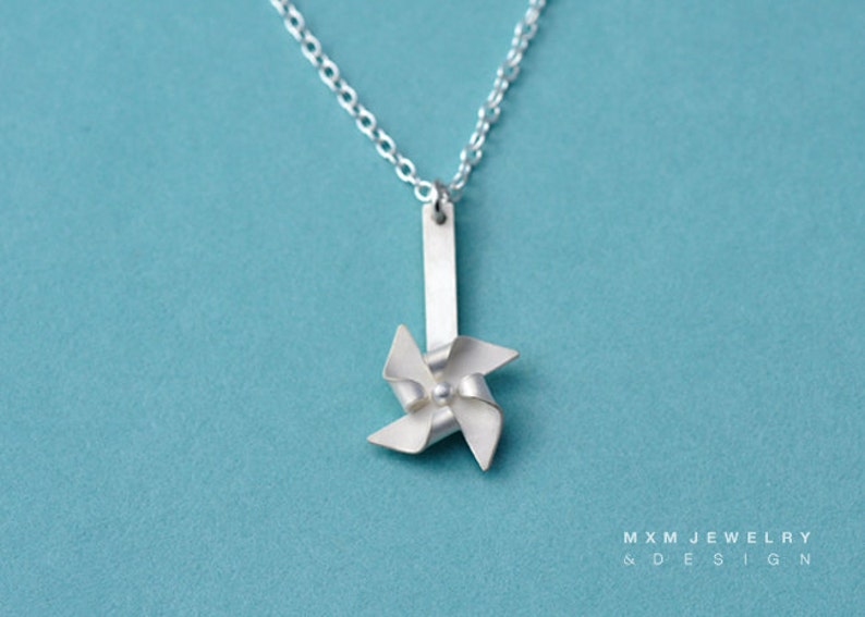 May include: A silver necklace with a small silver pinwheel pendant. The pinwheel has four blades and a small silver bead in the center.