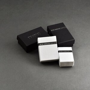 Puede incluir: Cuatro peque&ntilde;as cajas rectangulares, dos negras y dos blancas, con el texto "MWM JEWELRY EDITION" impreso en las cajas negras y "MWM JEWELRY & DESIGN" impreso en las cajas blancas.