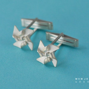 Puede incluir: Un par de gemelos de plata con un dise&ntilde;o de molino de viento. Los molinos de viento est&aacute;n hechos de plata y tienen un acabado de esmalte blanco.