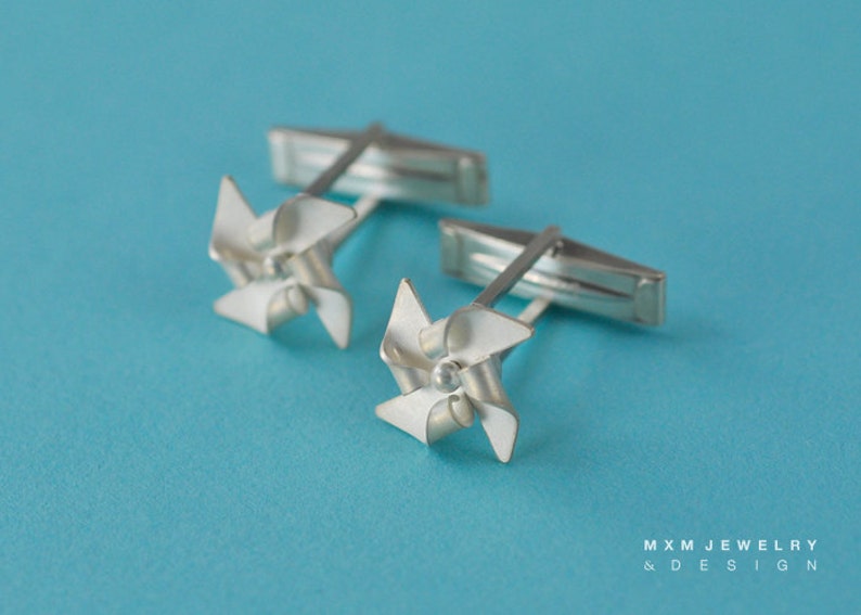 Puede incluir: Un par de gemelos de plata con un dise&ntilde;o de molino de viento. Los molinos de viento est&aacute;n hechos de plata y tienen un acabado de esmalte blanco.