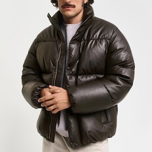 Peut inclure: Veste matelassée marron foncé avec un col montant et une fermeture éclair. La veste a un design matelassé et un aspect brillant semblable au cuir. Les manches sont longues et la veste semble chaude et isolée.