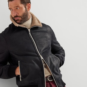May include: Black leather bomber jacket with a shearling collar and a ribbed knit hem and cuffs. The jacket features a silver zipper closure and two side pockets. The model is wearing a cream-colored turtleneck sweater.