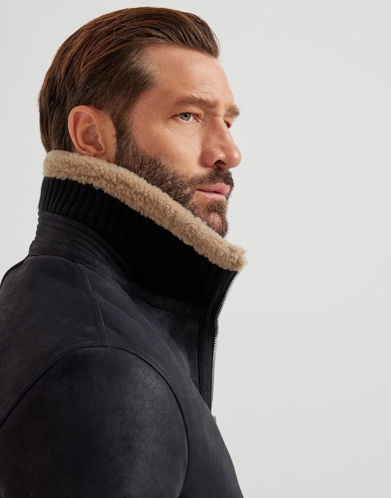May include: A black leather jacket with a high, ribbed collar and a tan shearling lining. The jacket has a zipper closure and a textured surface. The model is wearing the jacket.