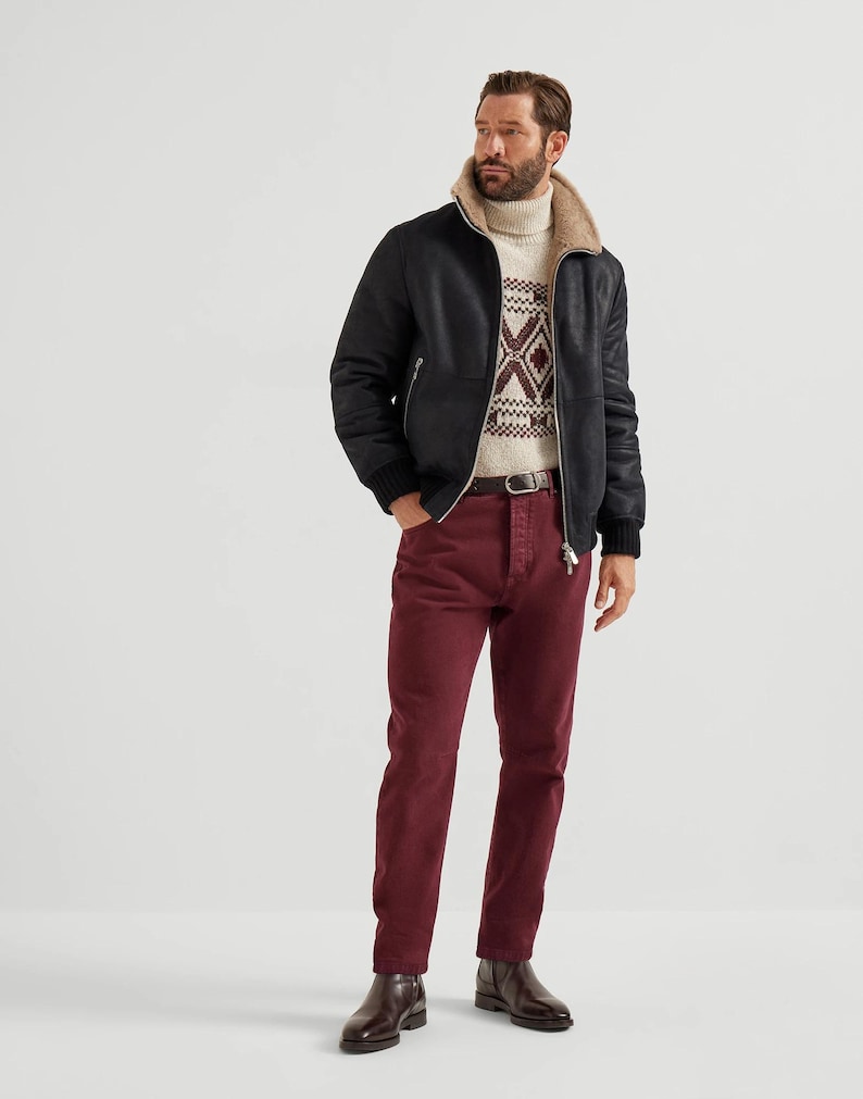 May include: A black leather jacket with a beige shearling collar and a patterned sweater. The person is wearing burgundy pants and brown boots. The jacket has a zipper closure and ribbed cuffs.