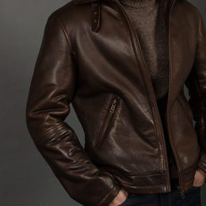 Puede incluir: Chaqueta de cuero marr&oacute;n con cuello de borrego. La chaqueta tiene cierre de cremallera, un bolsillo en el pecho y un dobladillo acanalado. El modelo lleva un jersey de cuello alto marr&oacute;n y vaqueros azul oscuro.