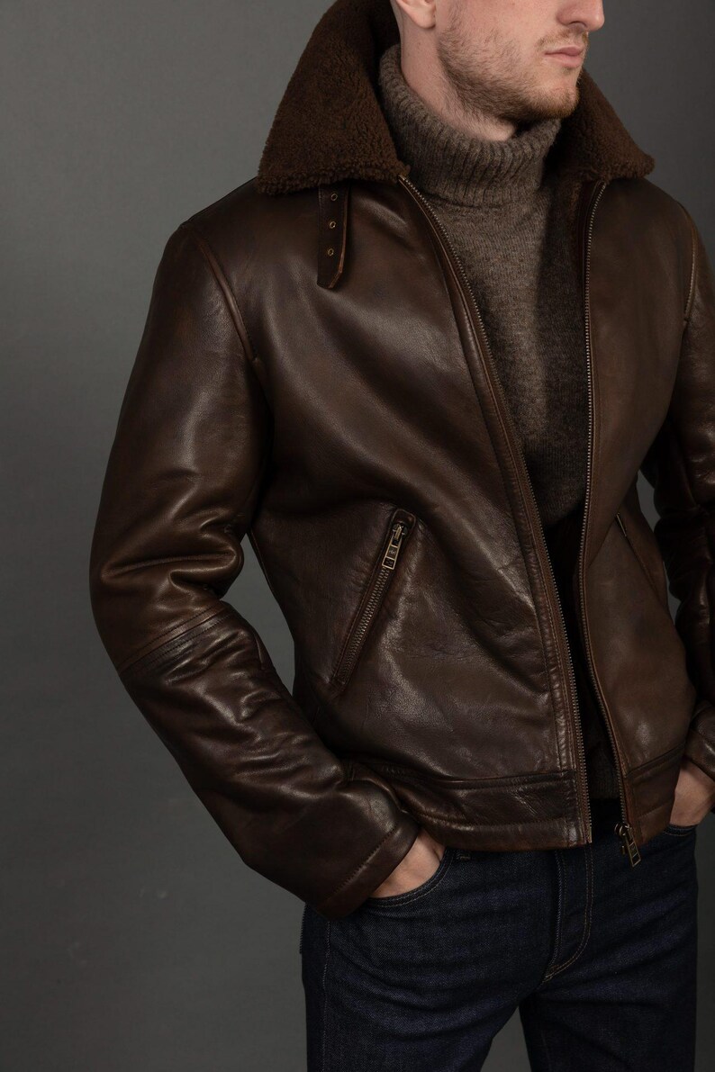 Puede incluir: Chaqueta de cuero marr&oacute;n con cuello de borrego. La chaqueta tiene cierre de cremallera, un bolsillo en el pecho y un dobladillo acanalado. El modelo lleva un jersey de cuello alto marr&oacute;n y vaqueros azul oscuro.