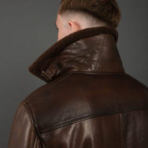 Puede incluir: Chaqueta de cuero marr&oacute;n con cuello de borrego. La chaqueta tiene un dise&ntilde;o cl&aacute;sico con una correa de hebilla en el cuello y costuras visibles. El cuero es de un color marr&oacute;n oscuro intenso y el borrego es de un marr&oacute;n m&aacute;s claro.