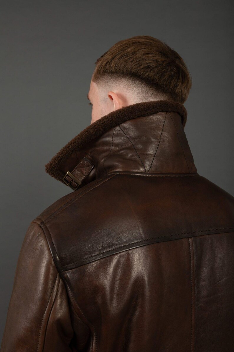 Puede incluir: Chaqueta de cuero marr&oacute;n con cuello de borrego. La chaqueta tiene un dise&ntilde;o cl&aacute;sico con una correa de hebilla en el cuello y costuras visibles. El cuero es de un color marr&oacute;n oscuro intenso y el borrego es de un marr&oacute;n m&aacute;s claro.