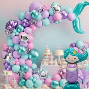 Könnte beinhalten: Ein Party-Dekorationsset zum Thema Meerjungfrau. Das Set enthält einen Ballonbogen in Pastellfarben, einen ballonförmigen Meerjungfrau und dekorative Kuchen. Der Ballonbogen hat rosa, lila und türkisfarbene Ballons mit silbernen Sternakzenten. Der Meerjungfrauen-Ballon hat einen lila Schwanz und türkisfarbenes Haar.