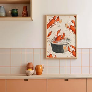 Op de afbeelding: Een ingelijste illustratie van rode kreeften in een pan met glazen champagne. De illustratie is op een witte achtergrond met een houten lijst.