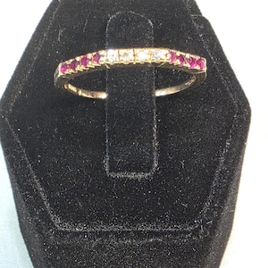 Peut inclure: Une bague en or avec une rangée de pierres précieuses alternées. La section centrale contient trois pierres blanches transparentes, flanquées de chaque côté de quatre pierres rouges vives, créant un motif symétrique sur la moitié supérieure.