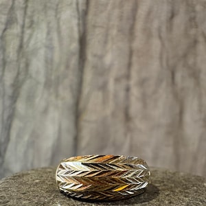 May include: A silver ring with a textured chevron pattern. The ring is wide and has a rounded shape.
