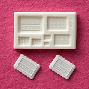 May include: White silicone mould with eight different shapes for making biscuits. The mould has a label that says "I love to bake". Two white biscuits with the word "Biscuit" printed on them are shown next to the mould.