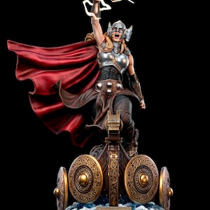 May include: A statue of Thor, the Mighty Thor, holding a hammer aloft. The figure is clad in silver armor and a red cape, standing on a base with shields and the word "Thor". The statue is set against a black background.