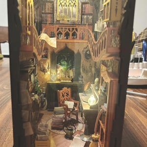 May include: A miniature wooden dollhouse with a detailed interior, featuring a library with bookshelves, a desk with a chair, and a staircase. The dollhouse is lit from within, creating a warm and inviting atmosphere.