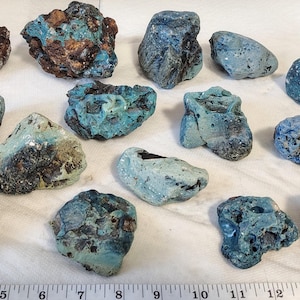 May include: An assortment of irregularly shaped rocks with a mix of blue, teal, and brown hues. The rocks vary in size and texture, some with porous surfaces. A ruler is at the bottom of the image, with measurements in inches.