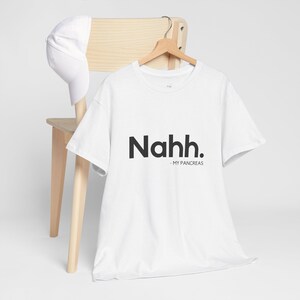 May include: White t-shirt with black text that reads "Nahh. - MY PANCREAS" hanging on a wooden chair.