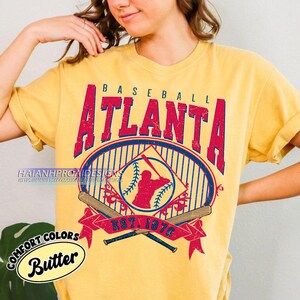 May include: A yellow t-shirt with a vintage baseball graphic featuring the text "BASEBALL ATLANTA EST. 1876" and a silhouette of a baseball player. The graphic is in red, blue, and white.