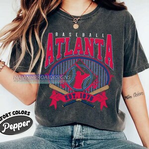 May include: A gray t-shirt with a vintage baseball graphic featuring the text "BASEBALL ATLANTA EST. 1876". The graphic is in red, blue, and white with a baseball player silhouette.