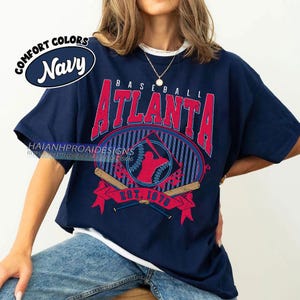 May include: A navy blue t-shirt with a white underlay. The shirt features a vintage-style baseball graphic with the text "BASEBALL ATLANTA EST. 1976" in red and white.