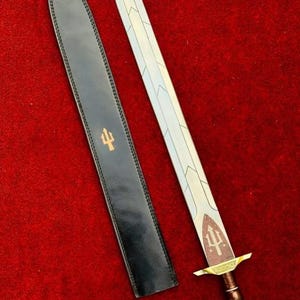 May include: A double-edged sword with a silver blade featuring a central ridge and chevron engravings. The hilt has a brown grip, a gold-toned crossguard, and a pommel. A black leather scabbard with a gold trident emblem is positioned beside it.